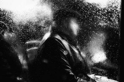 Man in train seen through wet window during rainy season at night