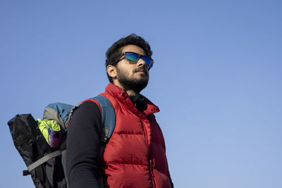 Low angle view of young man standing against clear blue sky