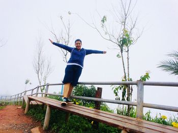 Low angle view of woman with arms outstretched standing by railing against clear sky