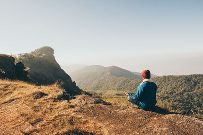 Rear view of man sitting on mountain against clear sky