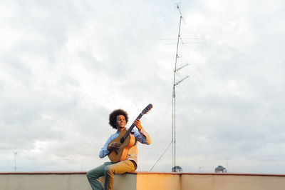 Low angle view of young man holding umbrella against sky