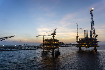 Cranes at commercial dock against sky during sunset