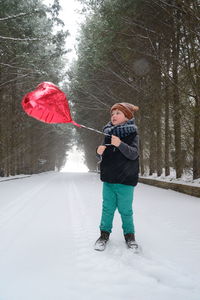 Boy holding heart shape balloon on snow covered pathway