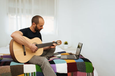 Man playing guitar while looking at laptop