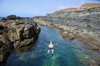 Rear view of person on rock by sea against sky