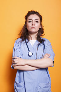 Portrait of female doctor holding stethoscope against yellow background