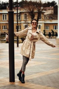 Full length portrait of smiling young woman playing with pole on footpath