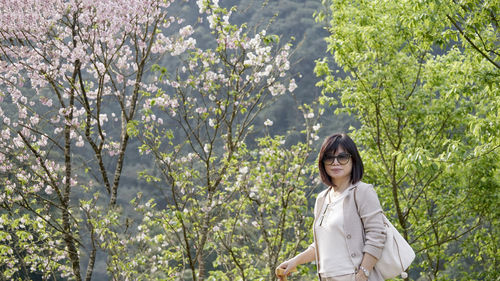 Young woman standing by plants against trees