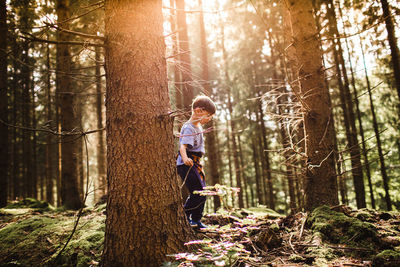 Side view of boy walking by trees in forest