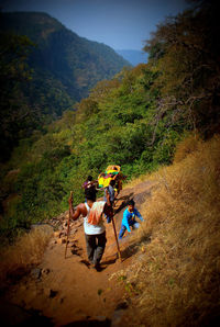 High angle view of men carrying woman on shoulders while moving down mountain