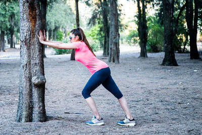 Full length of woman with pink flowers on tree trunk