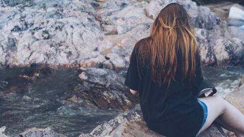 Rear view of woman sitting on rock by stream