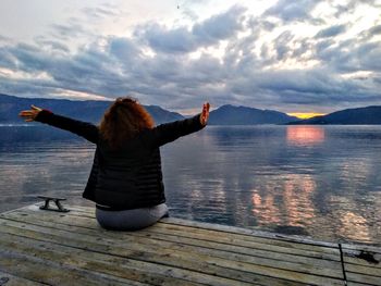 Rear view of woman with arms outstretched on lake against sky