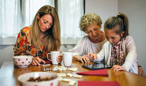 Girl with mother and grandmother using digital tablet on table at home