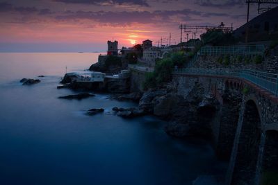 Buildings by sea against sky during sunset