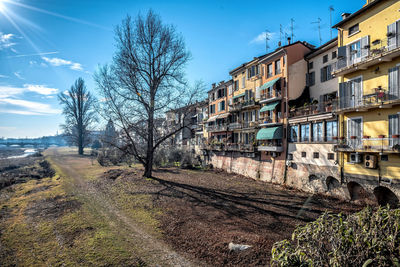 Bare trees by railroad tracks by buildings in city against sky