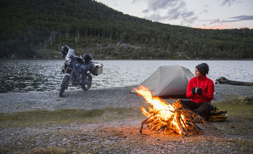 Woman enjoying campfire at camp next to still lake in tierra del fuego