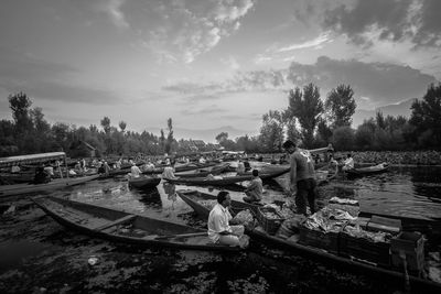 People sitting on riverbank against sky