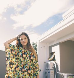 Portrait of woman with long brown hair standing in yard against sky