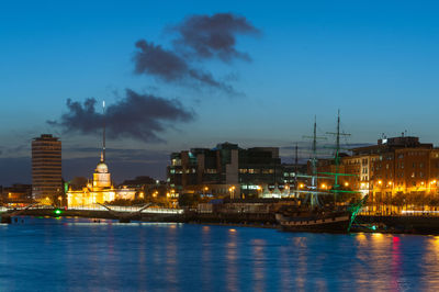 Illuminated buildings by river against sky at night