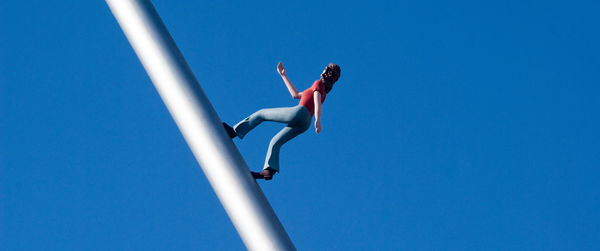 Low angle view of woman jumping against clear blue sky