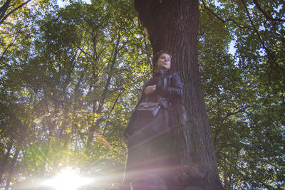 Low angle view of woman standing by tree in forest