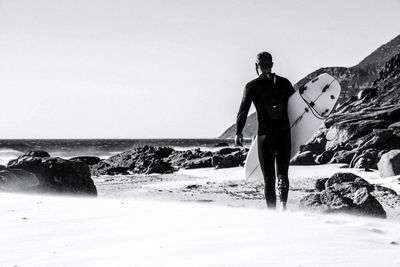 Rear view of man carrying a surfboard on beach