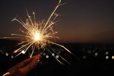 Close-up of hand holding illuminated sparkler against sky at night