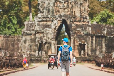 Rear view of young man with backpack walking towards built structure