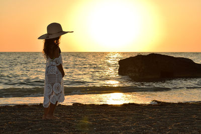 Woman standing on beach against sea during sunset