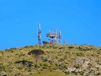 Low angle view of communication tower on hill against clear blue sky