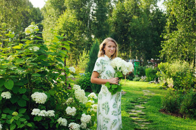 Portrait of smiling woman holding bouquet standing on grass outdoors