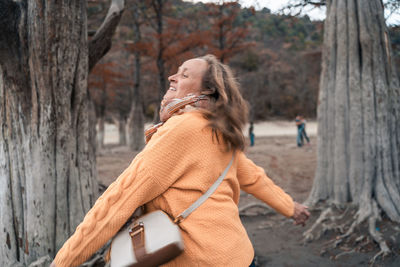 Side view of woman standing on tree trunk