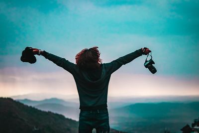 Rear view of woman with arms outstretched standing on mountain against sky