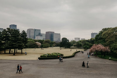 People in park by buildings against sky