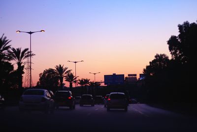 Cars on street against sky at sunset