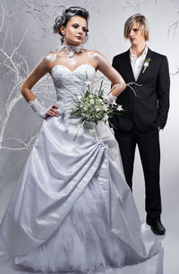 Bride and groom with bare trees standing against white background