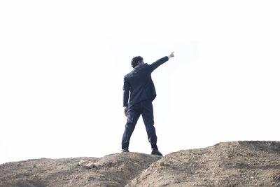 Rear view of man standing on rock against clear sky