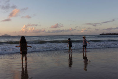 Women standing on beach against sky during sunset