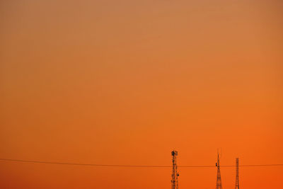 Low angle view of silhouette electricity pylon against orange sky