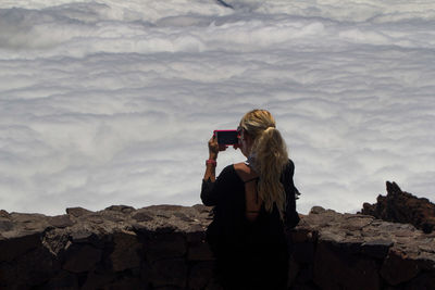 Rear view of woman photographing on rock the clouds below