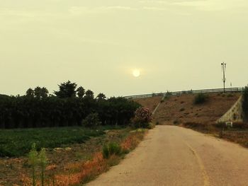 Empty road by trees against sky during sunset