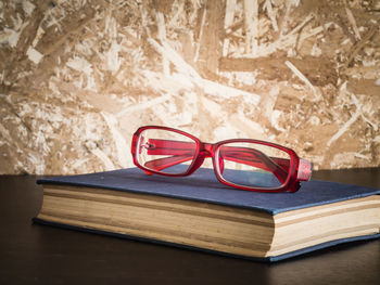 Close-up of book with eyeglasses on wooden table