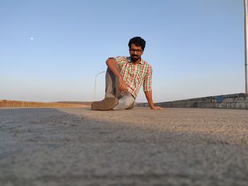 Full length portrait of boy sitting on land against clear sky