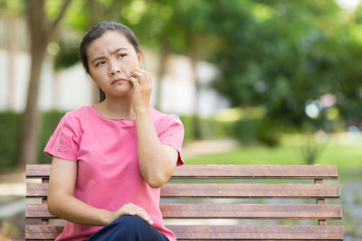 Young woman scratching cheek while sitting on bench at park