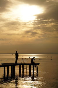 Silhouette people on pier by sea against sky