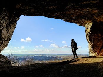 Rear view of man standing on rock against sky