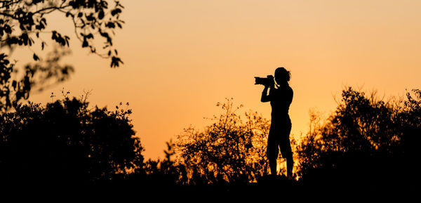 Silhouette man photographing on camera against sky during sunset