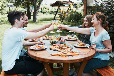 Friends making toast during summer picnic outdoor dinner in a home garden