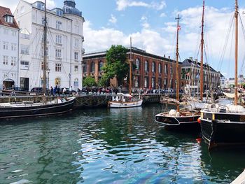 Sailboats moored on canal by buildings in city against sky